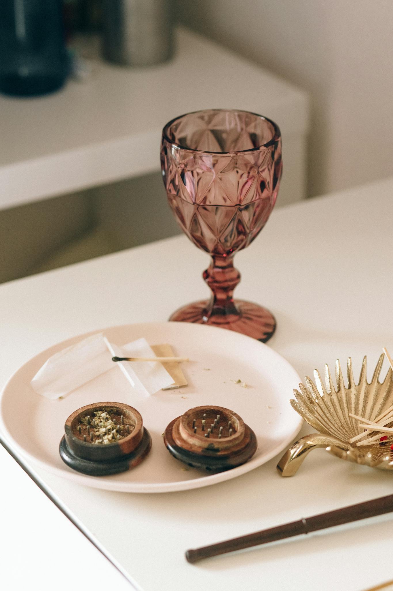 Elegant table setup featuring a pink glass goblet and cannabis rolling supplies, ideal for lifestyle photos.