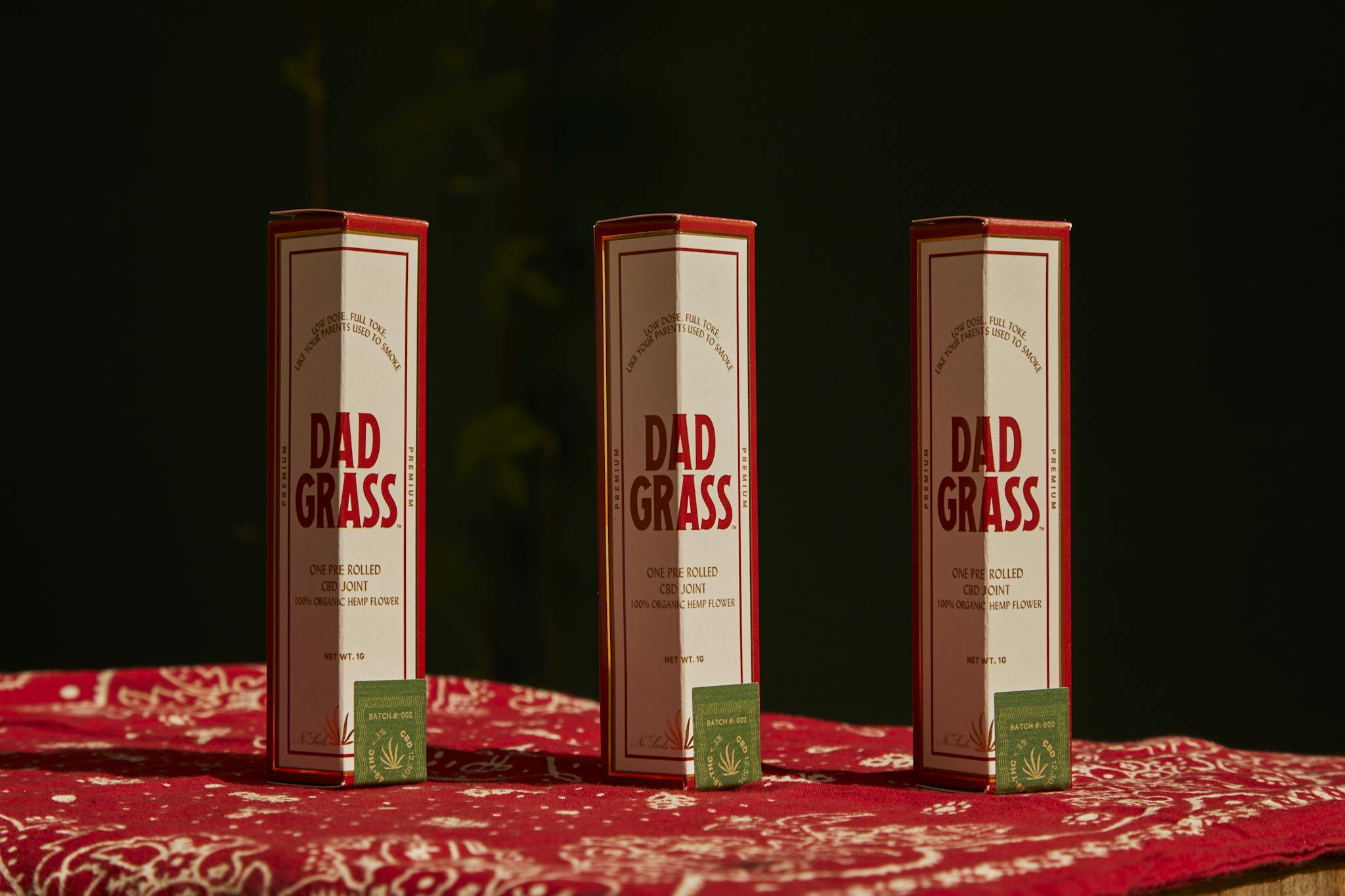 Stylish packaging of Dad Grass pre-rolled cannabis joints on a red patterned cloth.