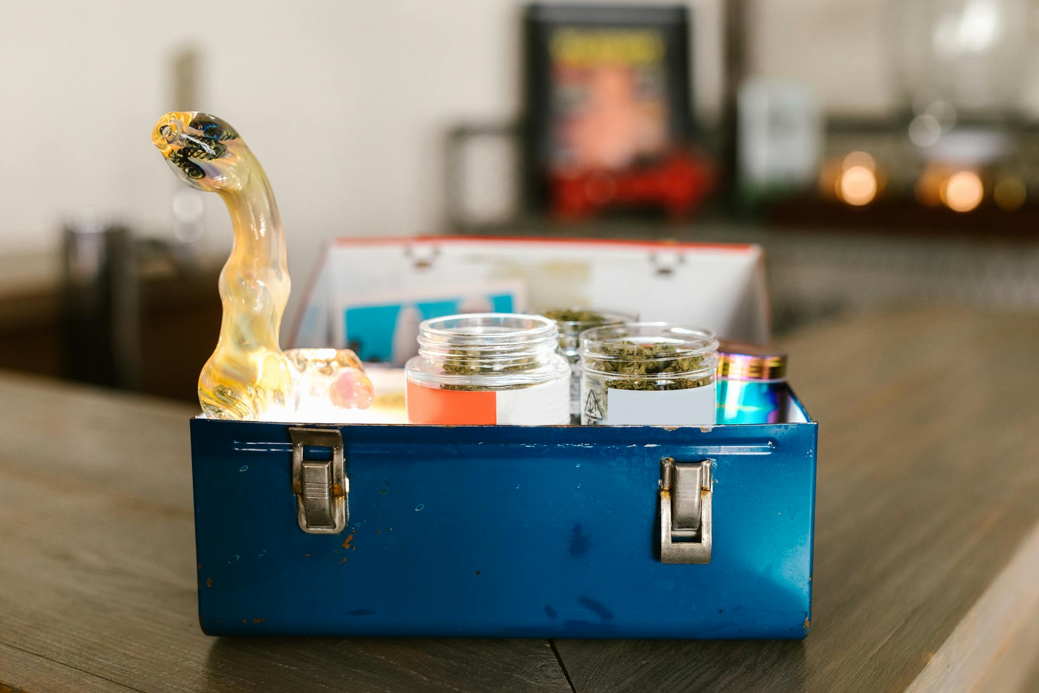 Vibrant blue storage box holding cannabis jars and a glass pipe, indoors.